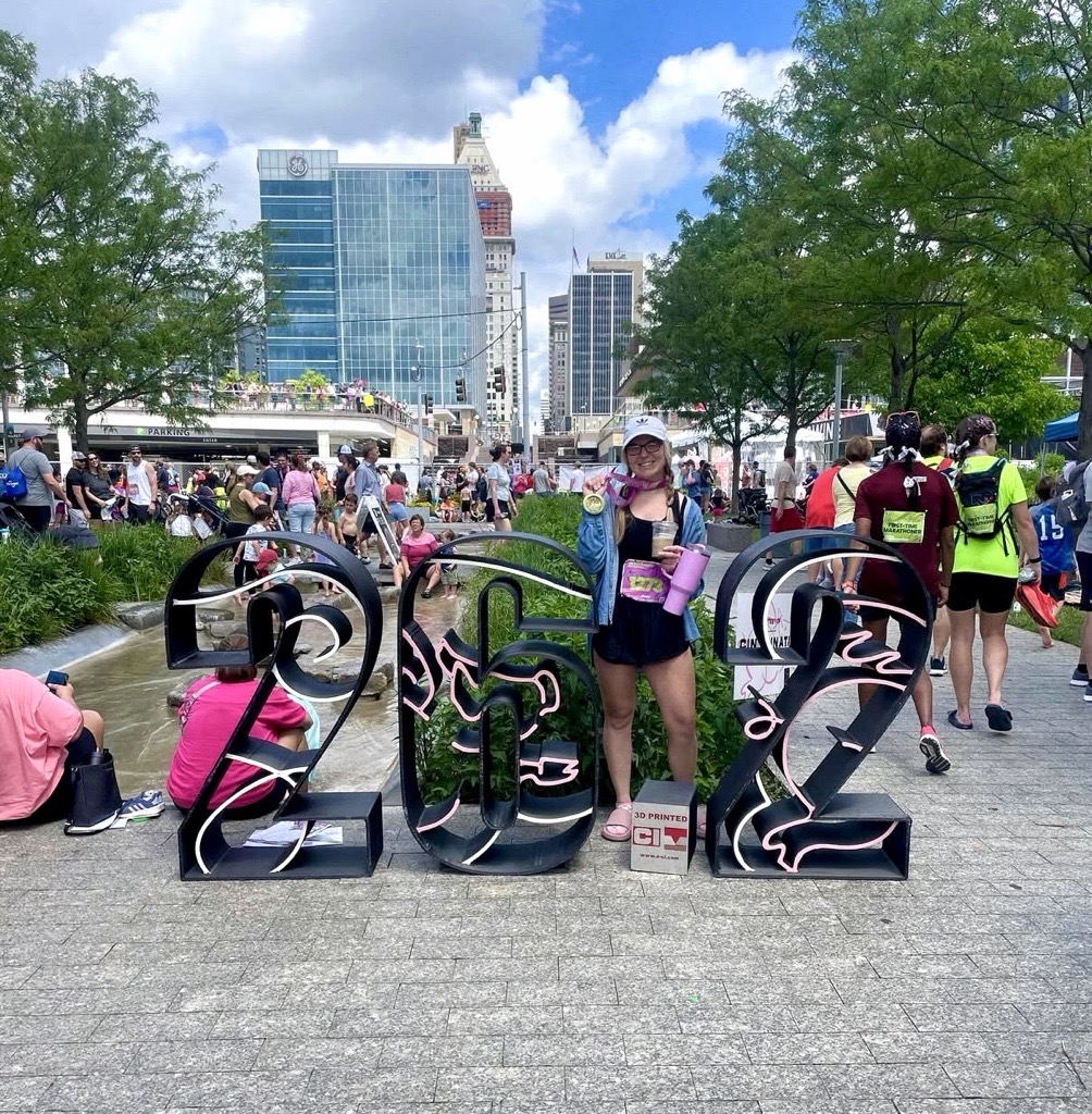 Marilee Cann holding her medal and smiling in front of the 26.2 sign after completing the 2024 Flying Pig Marathon in Cincinnati, Ohio.