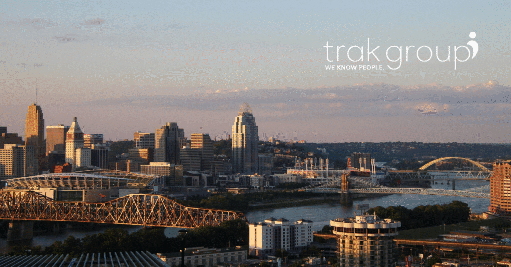 Cincinnati skyline at sunset with downtown buildings, river bridges, and the trak group logo in the upper right corner.